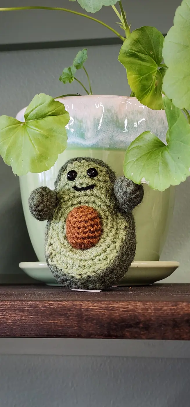 A crocheted avocado sitting in a plant pot